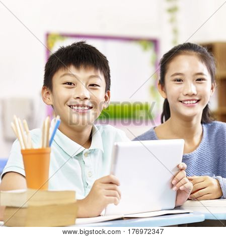 portrait of two happy asian primary school students looking at camera smiling.