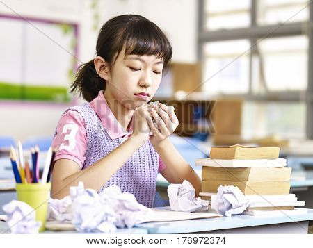 asian elementary school girl frustrated after several failed attempts while writing an essay.