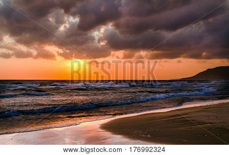 Sunrise over the sea, the rolling calm waves, sandy beach. Skay orange, pink clouds