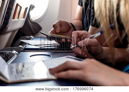 Male and female Passengers of Aircraft filling in Immigration Forms on tray Table holding Passports and Pens