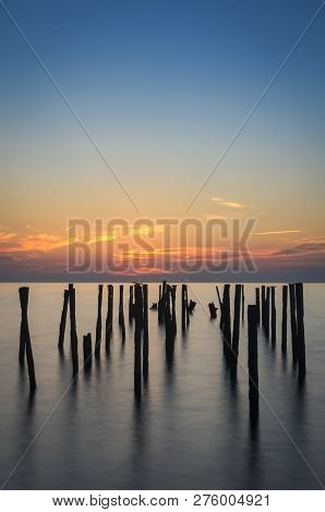Rusty Piles Stick Out Of The Water Against The Background Of The Sea Colorful Sunset. Long Exposure.