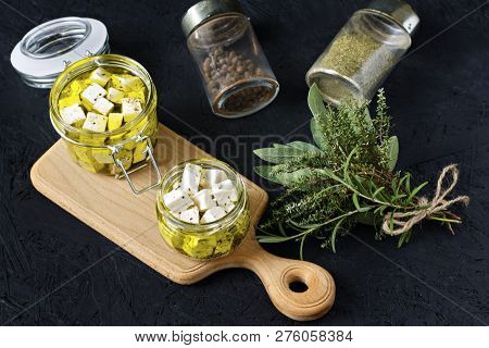 Marinated Feta In A Glass Jar And Spices On A Black Background.