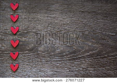 The Red Hearts Are Arranged Vertically On The Left On An Old Wooden Brown Dry Board. Valentines Day 