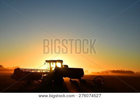 A Silhouette Image Of Agricultural Equipment In A Field At Sunset.