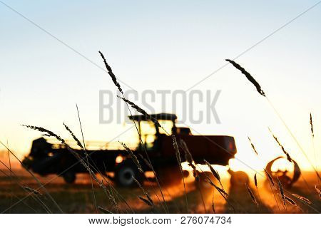 A Silhouette Image Of Agricultural Equipment In A Field At Sunset.