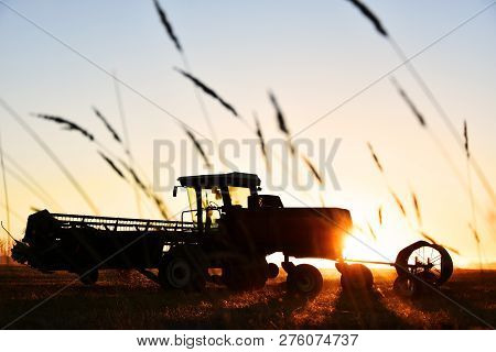 A Silhouette Image Of Agricultural Equipment In A Field At Sunset.