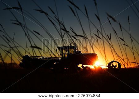 A Silhouette Image Of Agricultural Equipment In A Field At Sunset.