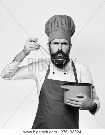 Cook With Strict Face In Burgundy Uniform Has Casserole With Ladle. Professional Cookery Concept. Ch