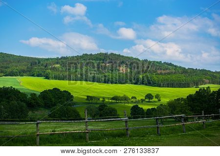 View Of Scenic Farmland, Rural Countryside, Green Grass, Yellow Field With Rape Plent, Bushes, A Hil