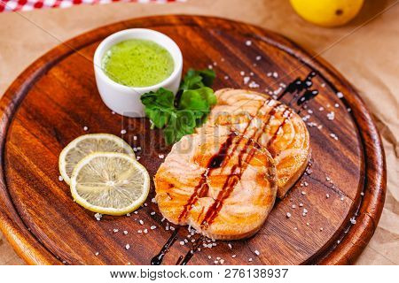 Grilled Fish Steak Served With Sauce And Lemon On Wooden Cutting Board. Close Up