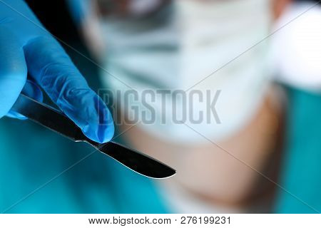 Surgeon Arms In Sterile Uniform Holding Sharp Knife While Operating Patient In Surgical Theatre Clos