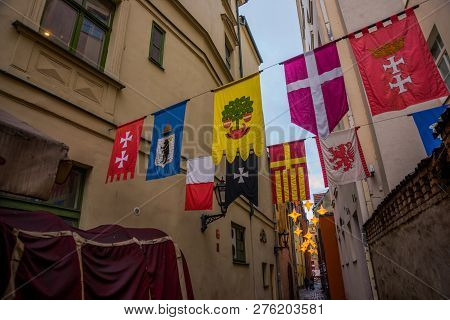 Flags Hanging On The Street Rozena Iela. Narrow Street In Old Town Riga, Latvia With Stars Garland. 