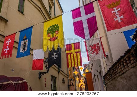 Flags Hanging On The Street Rozena Iela. Narrow Street In Old Town Riga, Latvia With Stars Garland. 