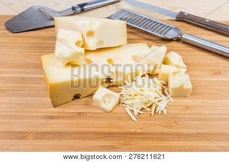 Partly Sliced And Grated Swiss-type Cheese With Large Holes On A Bamboo Wooden Cutting Board Against