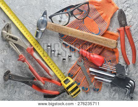 Working Tool On A Gray Concrete Surface. Work Gloves, Hammer, Nippers, Screwdriver, Pliers, Screwdri