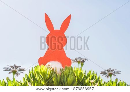 Creative Easter Concept Photo Of Red Paper Rabbit In The Chamomile Flowers And Green Grass On The Bl