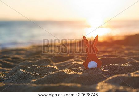 Creative Easter Concept Photo Of Red Paper Bunny On The Sand On The Beach At Sunset. Concept. Easter