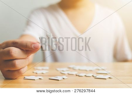 Hand Of Male Trying To Connect Pieces Of White Jigsaw Puzzle On Wooden Table. Healthcare For Alzheim