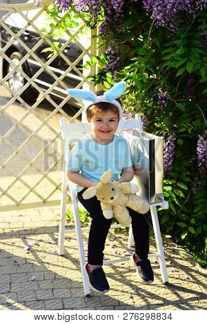 Gifts For Children. Young Smiling Kid Sits In White Chair On Vintage Background In Park And Holds Ra