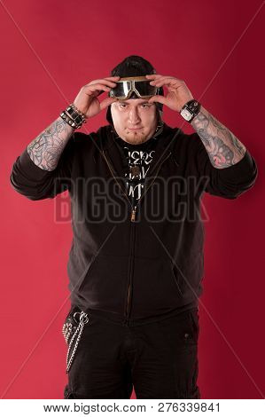 Portrait Of A Cool, Chubby Rocker In A Hoodie And Leather Aviator Helmet Isolated On Red. Half Lengt