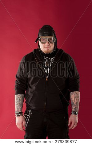 Portrait Of A Cool, Chubby Rocker In A Hoodie And Leather Aviator Helmeton Red Background. Half Leng
