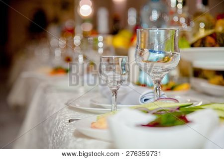 Festive Tableware With Glasses On A Table. Empty Glasses Stand Near Plates And Forks On Banquet Tabl