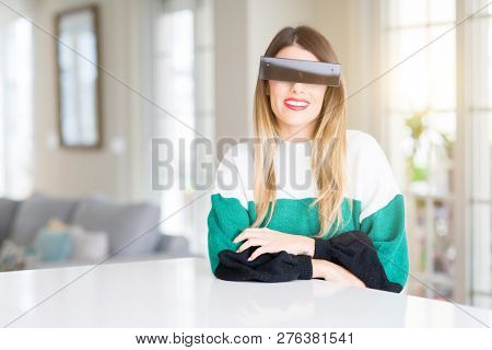 Young beautiful woman blindfold eyes with black censor band at home happy face smiling with crossed arms looking at the camera. Positive person.