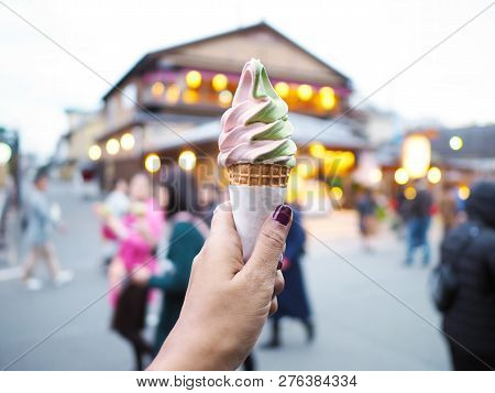 Woman Hand Holding Soft Cream Over Blurry Shopping Market Background With Bokeh At Arashiyama, Japan
