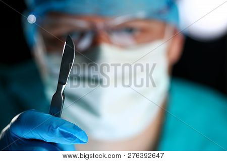Surgeon Arms In Sterile Uniform Holding Sharp Knife While Operating Patient In Surgical Theatre Clos