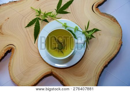 Marijuana Tea. Hemp Tea. Cannabis Tea in a White Tea Cup with a Marijuana Leaf and Stem with Flowers and Leaves on a Wooden Tree Stump serving tray. Room for text. 

