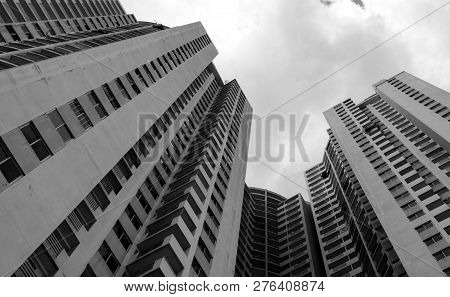 Bottom View Of Skyscraper Building Against Gray Sky And Clouds. Looking Up View In Apartment Buildin