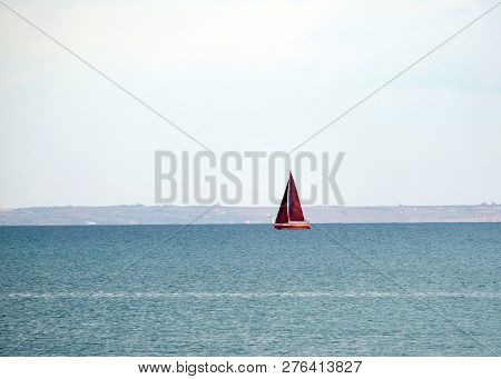 Landscape With Yacht With High Red Sails Floats Into The Sea In Calm Water Against The Backdrop Of T