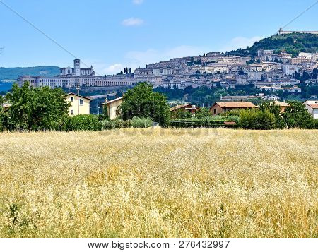 View Of The City Of Assisi, The Slope Of The Mountain Monte Subasio, Summer Clouds, Blue Sky