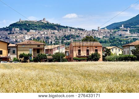 View Of The City Of Assisi, The Slope Of The Mountain Monte Subasio, Summer Clouds, Blue Sky