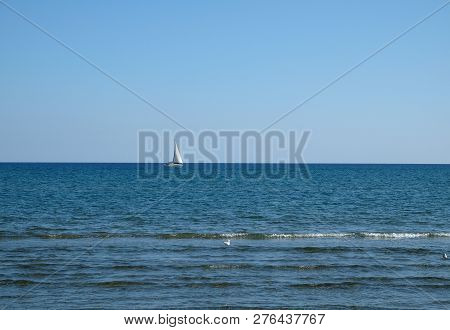 Landscape with yacht with high white sails floats into the calm open sea against clear skyline on bright sunny day