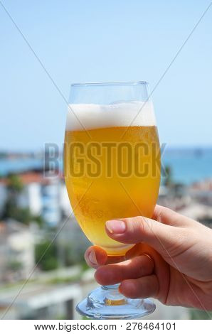 Hand Holding A Glass Of Beer In Beach Tropical Sea Background. Vacation Holiday Concept