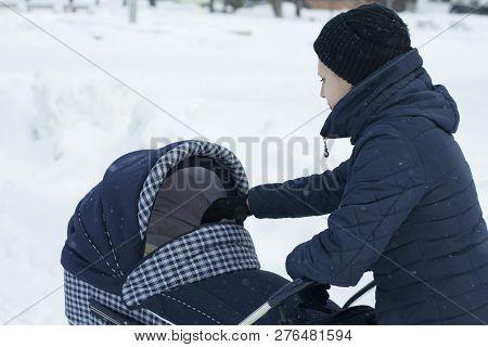 Mother Walks With A Stroller On A Snowy Winter Day