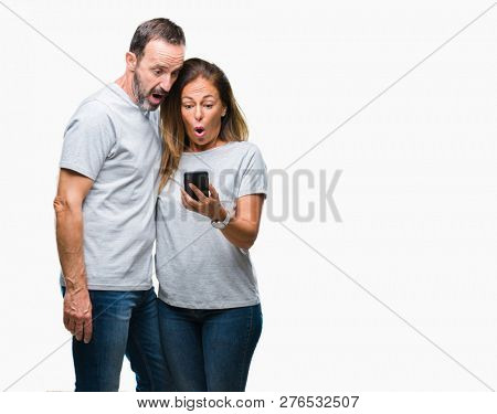 Middle age hispanic couple texting message on smartphone ver isolated background scared in shock with a surprise face, afraid and excited with fear expression
