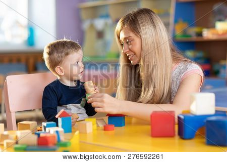 Cute Kindergarten Teacher And Baby Toddler Playing Educational Toys At Creche Or Nursery