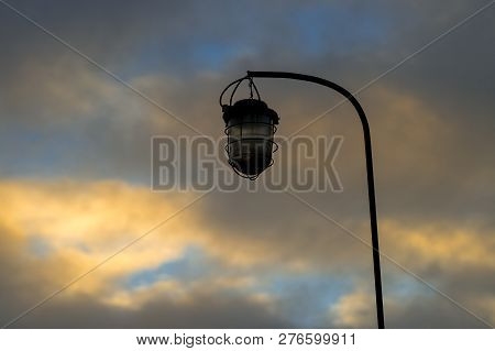 Old Street Lamp On The Background Of A Blocky Sky Suspended On An Iron Rusty Curved Tube