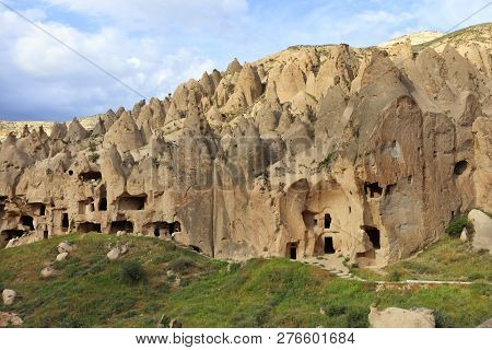 Old Antique Residential Caves On The Background Of The Conical Ridges Of Cappadocia And The Blue Clo