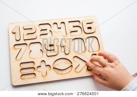 Wooden Puzzle With Numbers And Arithmetic Signs. Childrens Hand Takes The Figures From The Puzzle