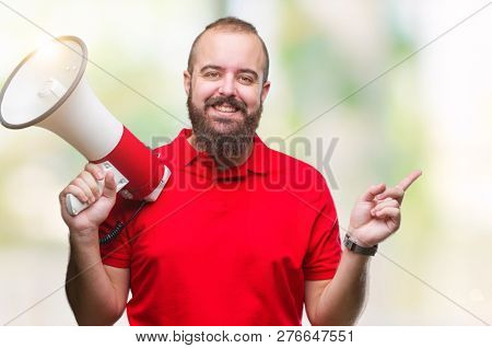Young caucasian man shouting through megaphone over isolated background very happy pointing with hand and finger to the side
