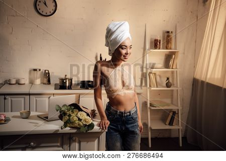 Beautiful Smiling Asian Girl In Lace Bralette, Jeans And Towel On Head Leaning At Table With Rose Fl