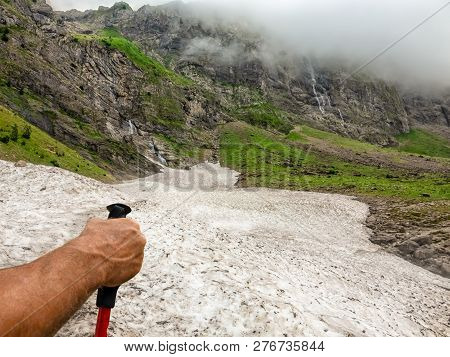 A Tourist's Hand Before Crosses A Glasier In Mountain Valley With Grand Waterfalls..