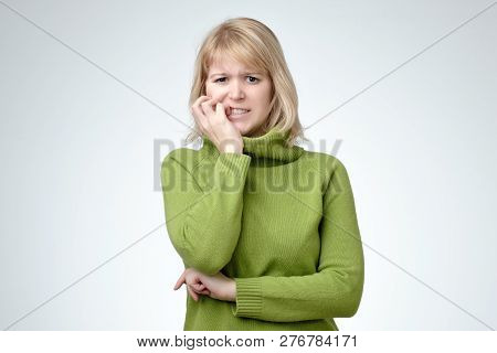 Girl With Puzzled Expression, Bites Finger Nails In Puzzlement, Looks Anxiously At Camera