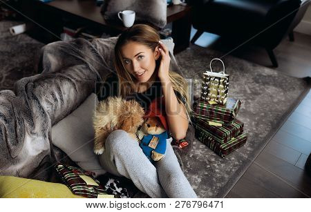 Attractive Blonde Girl Celebrating Winter Holidays At Home With Her Small Doggy, Playing And Pet Him