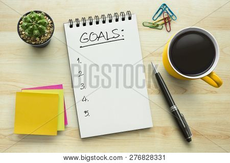 Top View Notebook With Goals List. Notepad On Office Table With A Cup Of Coffee, Plant, Stationery A