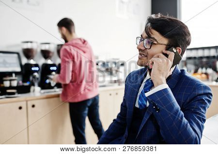 Stylish Indian Business Man On Suit And Glasses Sitting At Cafe And Speaking On Phone.
