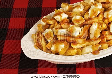 Poutine Plate On A Red And Black Tartan Tablecloth. Meal Cooked With French Fries, Beef Gravy And Cu